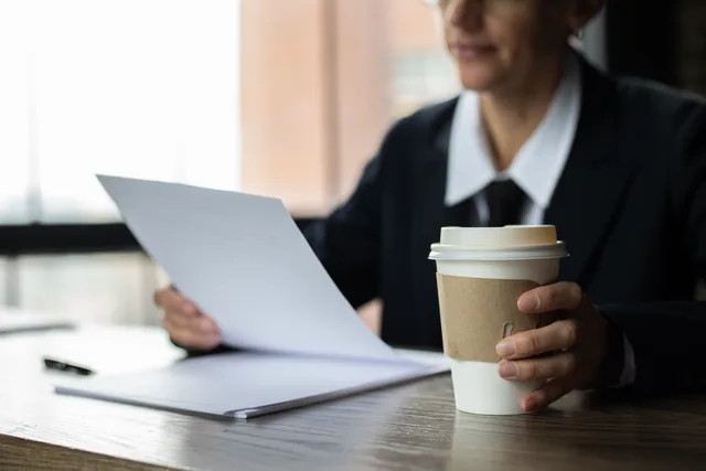 Focused businesswoman examining documents with a disposable coffee cup on a wooden desk. Franchise opportunities advertising rules: testing an earnings claim