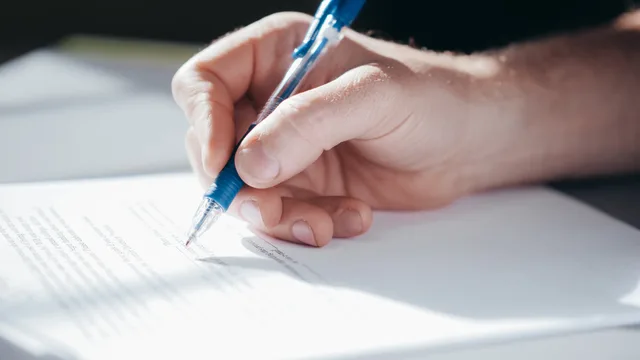 A detailed shot of a hand writing with a blue pen on a piece of paper. Franchise attribution methods: choosing the right design for a change